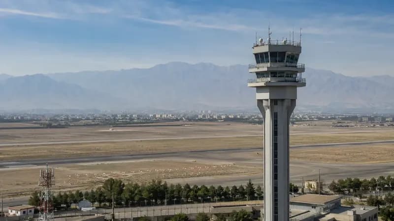 برج مراقبت فرودگاه در کنار باند پرواز با رشتهکوه در پسزمینه
